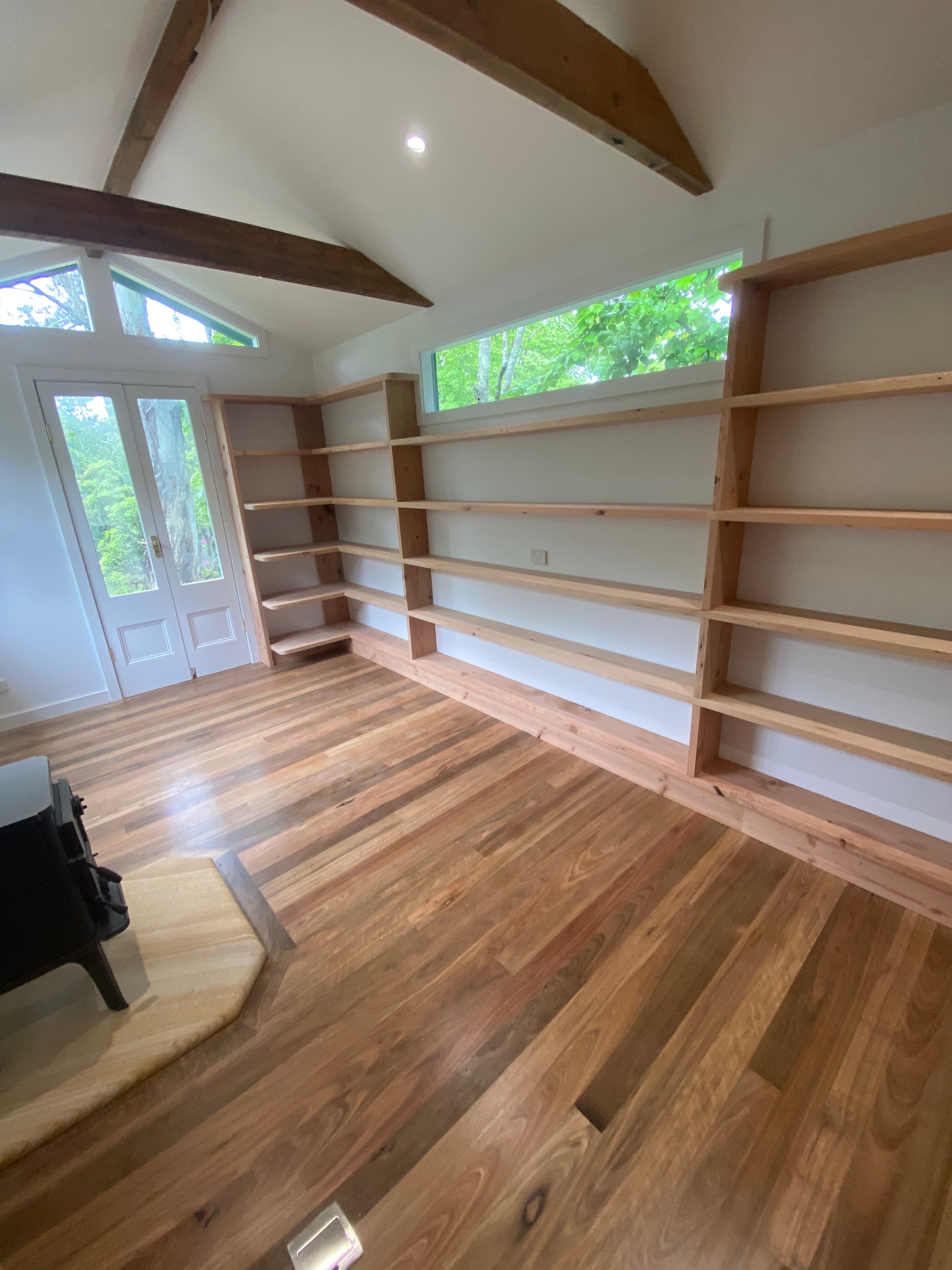 Wooden bookshelves in a room with wooden flooring and large windows.